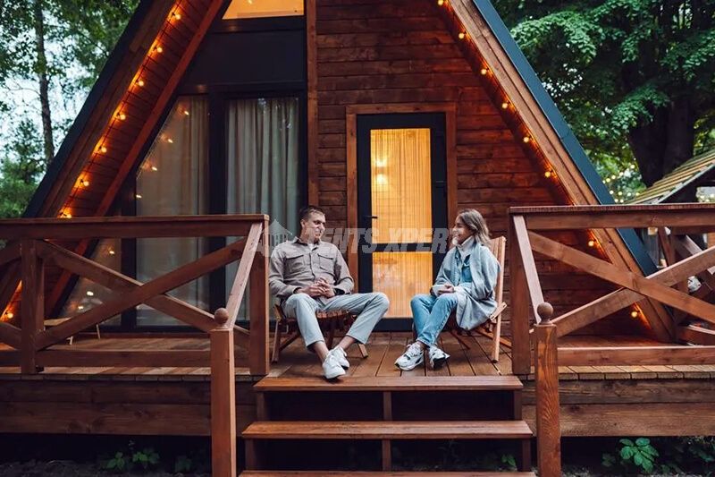 A man and a woman are chatting on the platform in front of the wooden house